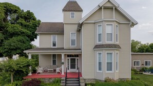 A two-story house with a covered porch, a front door, and a small staircase leading to the entrance. - Event Rental 10BR/10BA Sleeps 31 B&B Near The Lake (Marblehead)