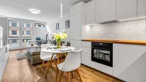Une cuisine moderne avec des armoires blanches, un four noir et un plan de travail en bois. On y trouve un coin repas avec une table et des chaises blanches, ainsi qu'un vase rempli de fleurs.