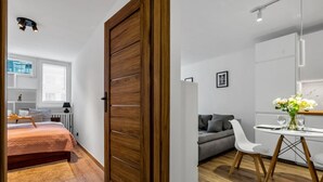 Une chambre moderne avec une armoire en bois, un lit recouvert d’une couverture rose, une table de chevet avec une lampe et une fenêtre avec des stores.