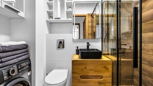 Une salle de bain moderne équipée d’un lave-linge, de toilettes, d’un meuble-lavabo en bois et d’une cabine de douche en verre.