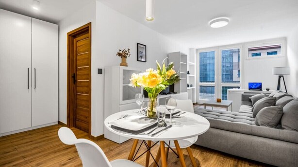 Un salon moderne avec un canapé gris, une table à manger dressée avec de la vaisselle blanche et une porte en bois.