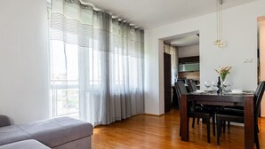 Ein modernes Wohnzimmer mit einem grauen Sofa, Holzboden, einem Esstisch für vier Personen und einer Küche im Hintergrund.