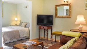 Una habitación de hotel con una cama, un televisor sobre un mueble de madera, un sofá, una mesita con un periódico y una lámpara.