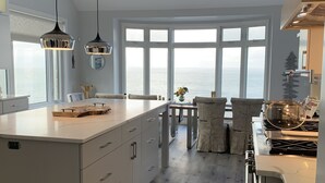 Una cocina moderna con una isla grande, luces colgantes y vistas al mar a través de amplios ventanales.