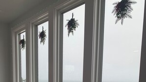 Una habitación con un ventanal grande con vistas a una playa nevada, una cama con ropa de cama estampada y piñas decorativas.