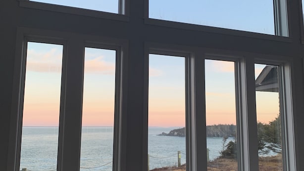 Una habitación con amplios ventanales arqueados que dan a una masa de agua y una costa lejana.