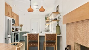 A modern kitchen with wooden cabinets, a central island with bar stools, a built-in oven, and pendant lighting.