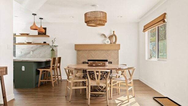 A modern kitchen with a marble countertop, wooden chairs, and a herringbone-patterned backsplash.