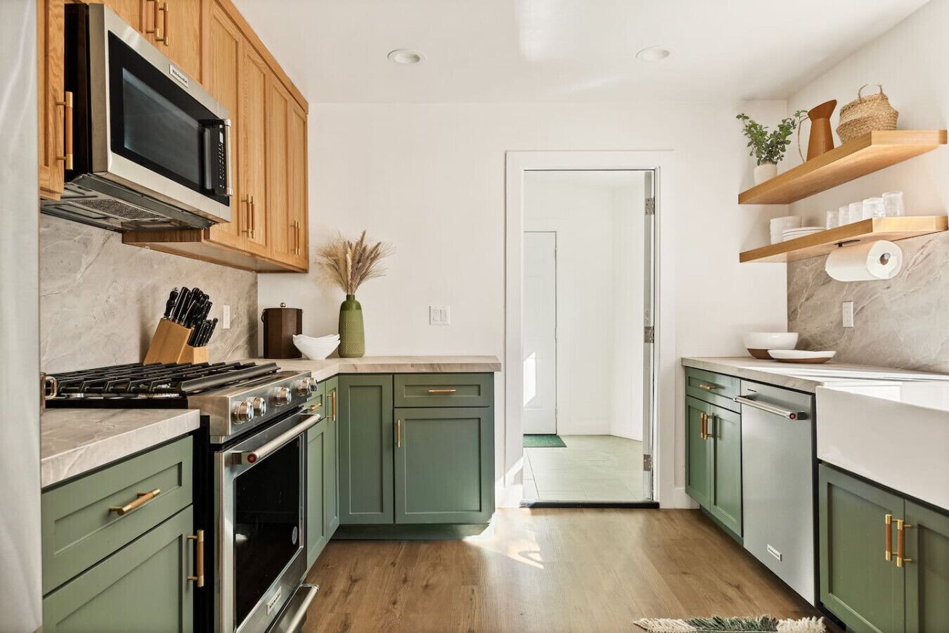A modern kitchen with green cabinets, a stainless steel stove, and wooden shelves.