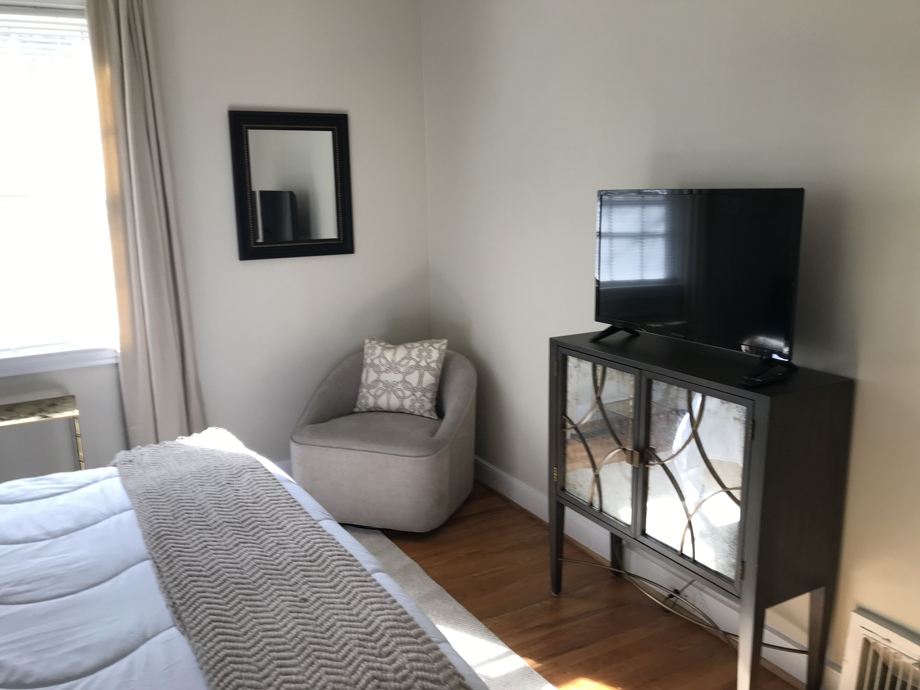 A bedroom with a bed, a grey armchair, a television on a cabinet, and a mirror on the wall.