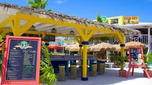 A beachside restaurant with a thatched roof, outdoor seating, and a menu board. - Downtown Nassau Oasis: Unit 1 (Nassau)