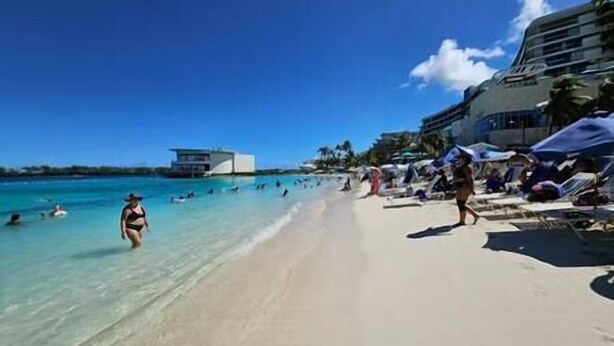 A beach with clear turquoise water, people swimming and sunbathing, and a modern building in the background. - Downtown Nassau Oasis: Unit 1 (Nassau)