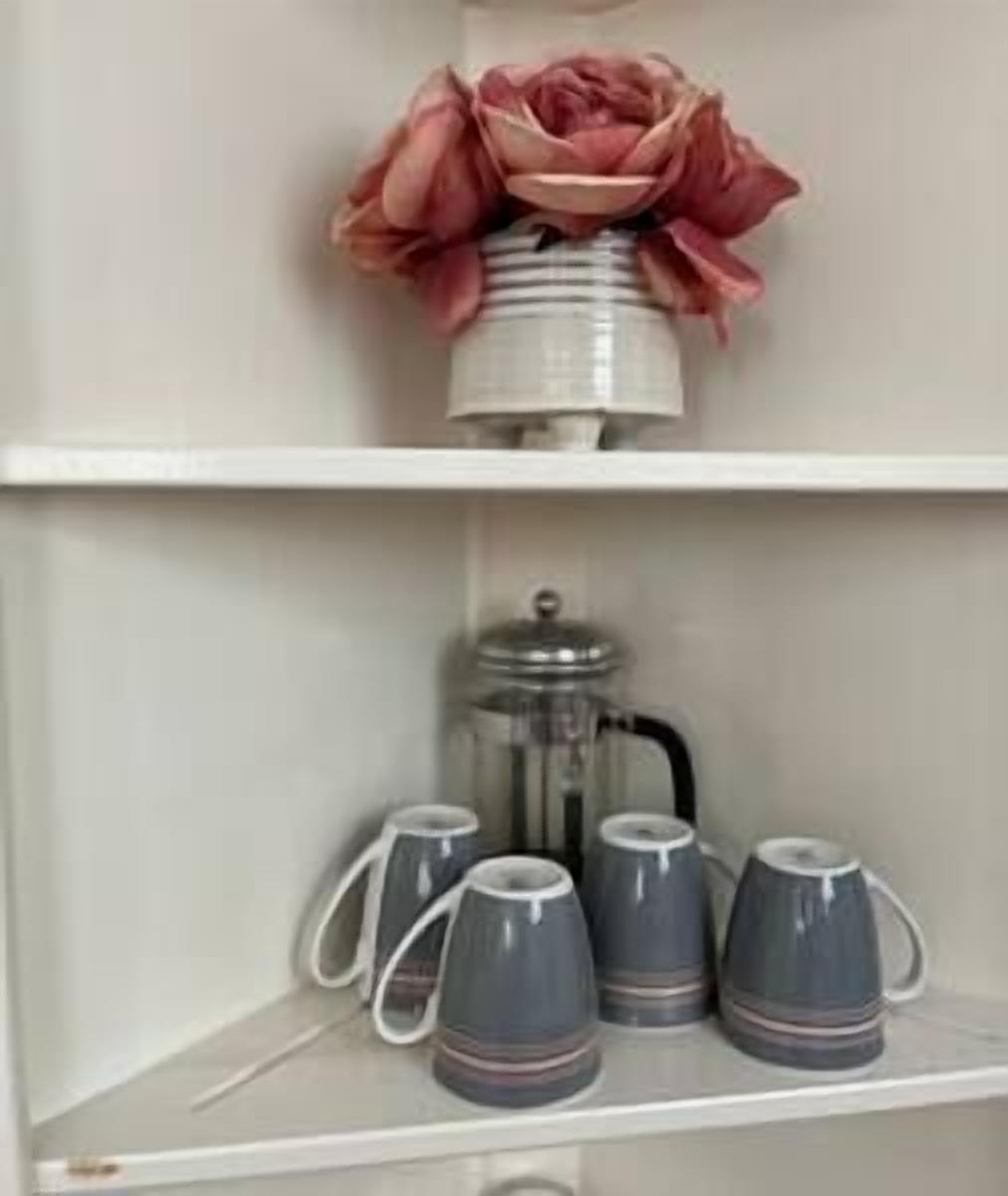 Una repisa con un arreglo floral rosa decorativo y una cafetera con cuatro tazas.