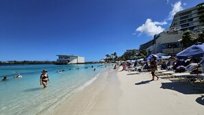 Una playa con agua turquesa cristalina, una orilla arenosa y un edificio con el rótulo "S.O.B. BAR" al fondo.