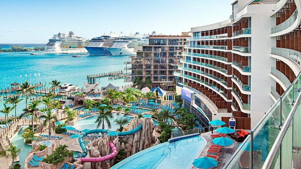 Un resort con área de piscina, toboganes acuáticos y vista a cruceros en el fondo.