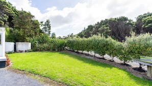 A well-maintained garden with a variety of trees and shrubs, a gravel path, and a white building with a flat roof. - Pearls Embrace - Mangawhai Heads Studio (Mangawhai Heads)