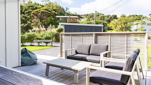 A deck with a table and two chairs, a green bag, and a wooden fence. - Pearls Embrace - Mangawhai Heads Studio (Mangawhai Heads)