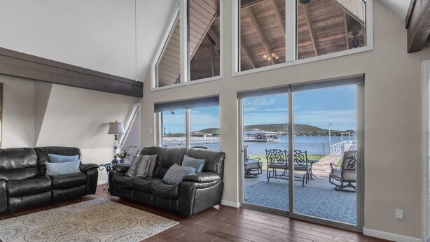 A spacious living room with a large window overlooking a dock and water, two leather sofas, and a staircase leading to an upper level.