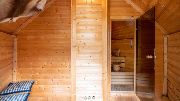 A wooden cabin interior with a sloped ceiling, a bed with checkered bedding, a small window, and a door leading to another room. - Ferienhaus am Waldrand Direkt am Sauerländer Höhenflug (Eslohe (Sauerland))