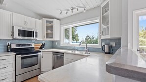 Eine moderne Küche mit weißen Schränken, Edelstahlgeräten, einem großen Fenster und Blick auf Bäume.