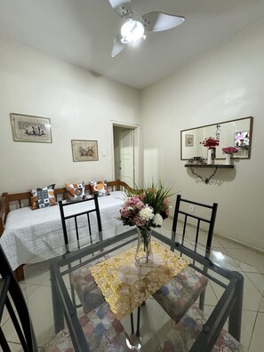A dining area with a glass table, chairs, a vase with flowers, a ceiling fan, and framed pictures on the walls. - Apartamento Copa Friends HIR 40 (Rio de Janeiro)