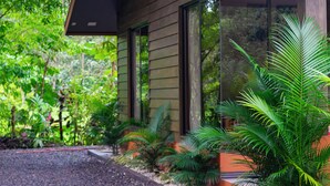 Een modern huis met grote ramen, omringd door weelderige begroeiing en tropische planten.