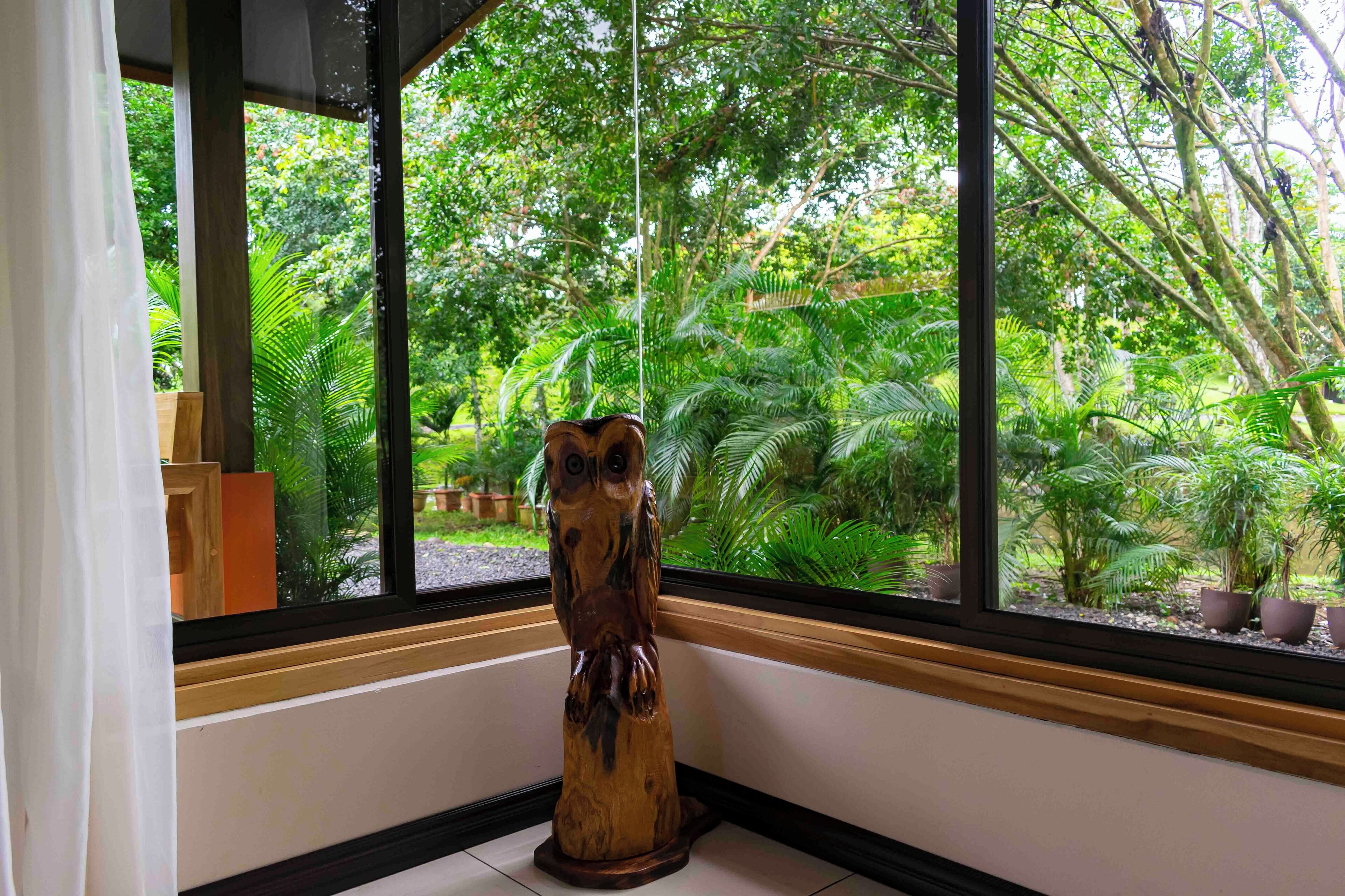 A wooden sculpture in a corner with a view of lush greenery through a window.
