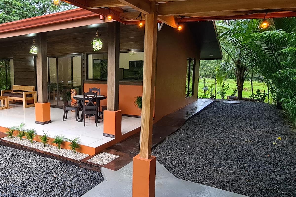Un espacio de estar al aire libre cubierto con mobiliario de madera y un sendero de grava que lo conecta.