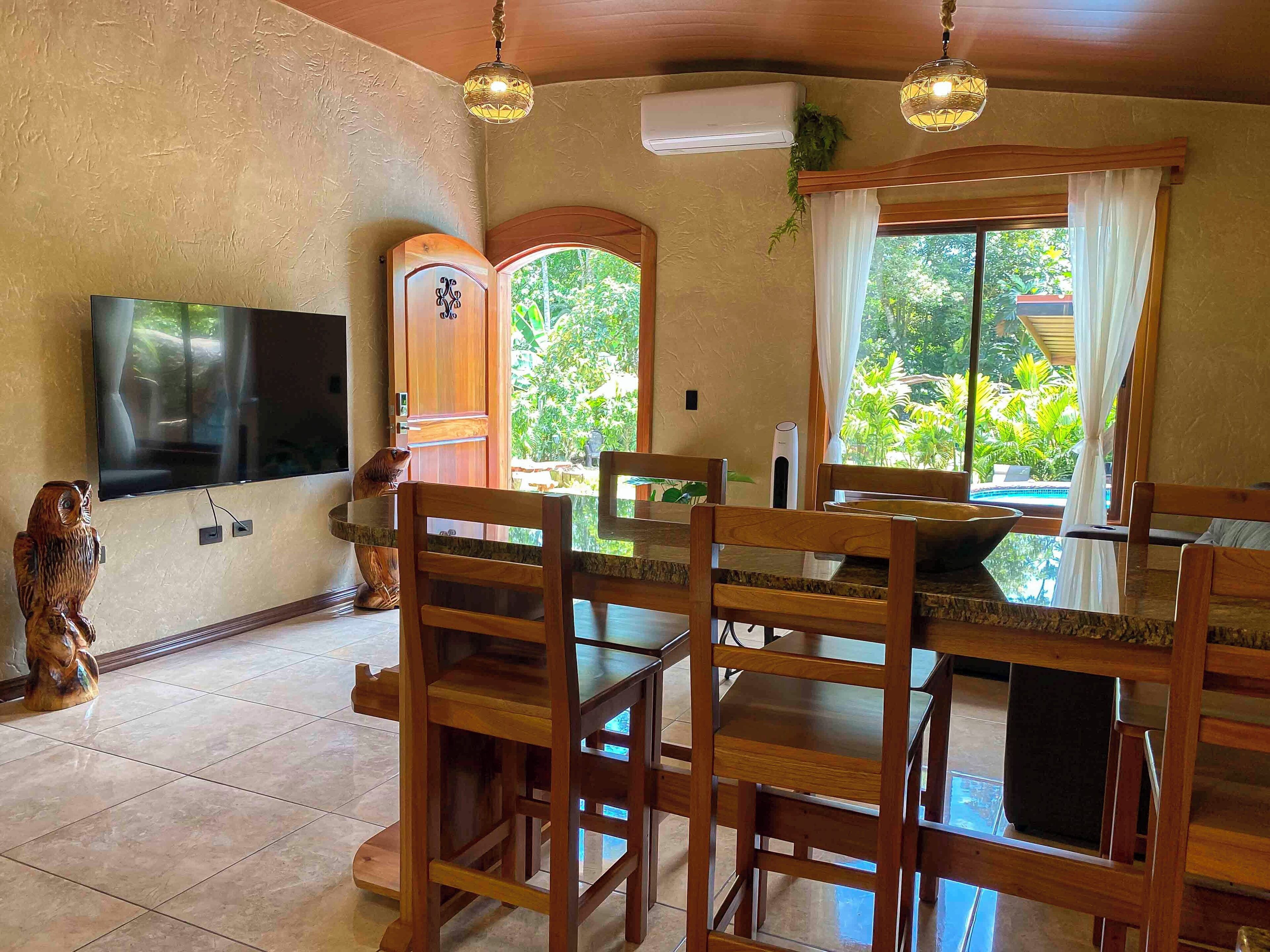 A dining area with wooden furniture, a flat-screen TV, and a view of the outdoors.