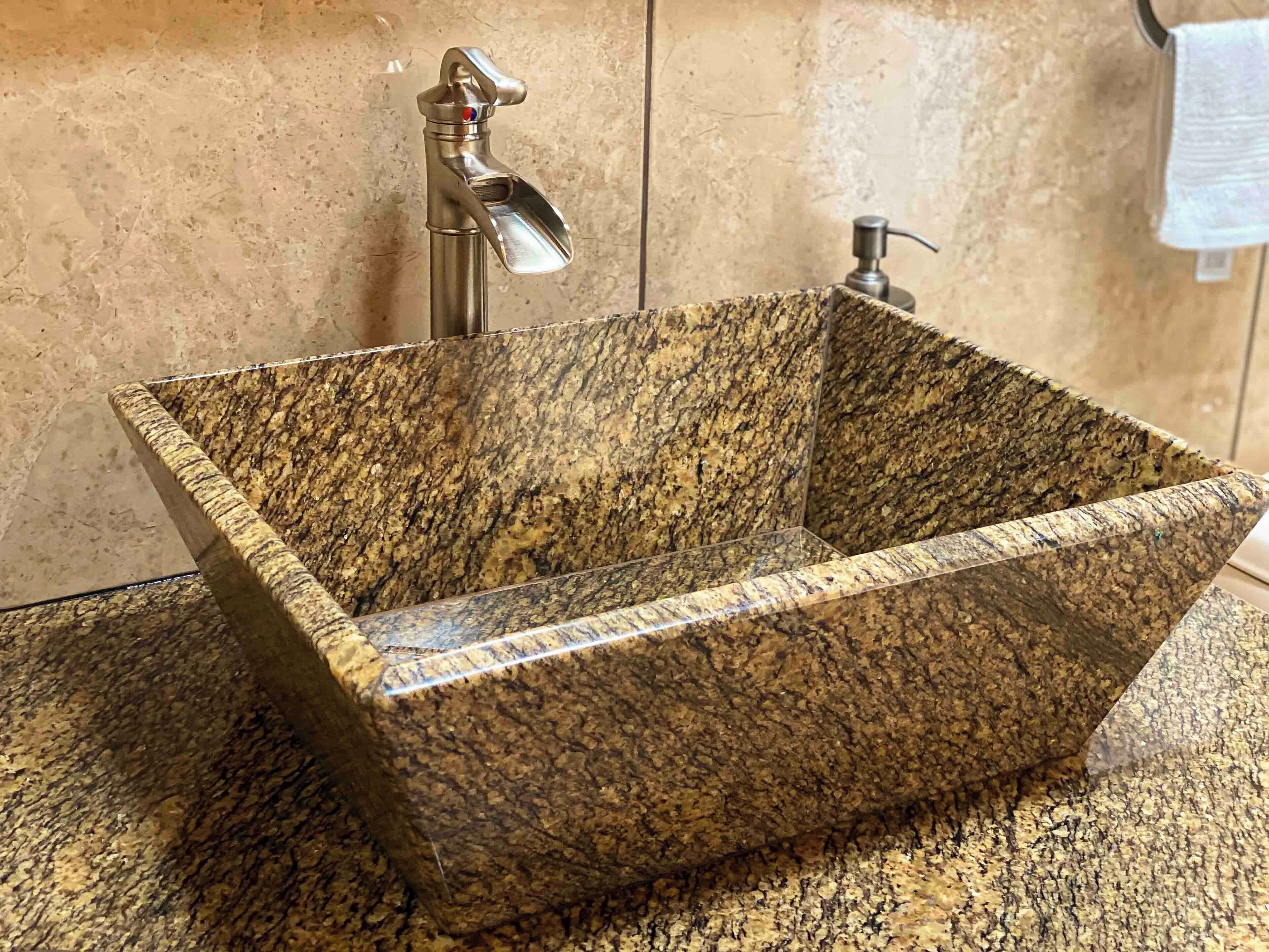 A rectangular granite sink with a faucet and soap dispenser in a bathroom.