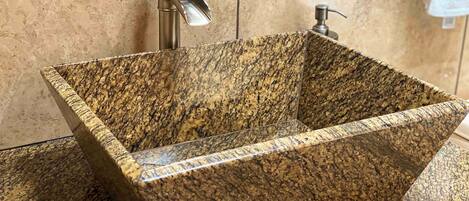 A rectangular granite sink with a faucet and soap dispenser in a bathroom.