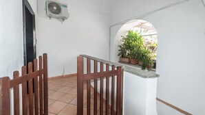 Un estrecho pasillo con suelo de baldosas, una puerta de madera, una pared blanca y un equipo de aire acondicionado.