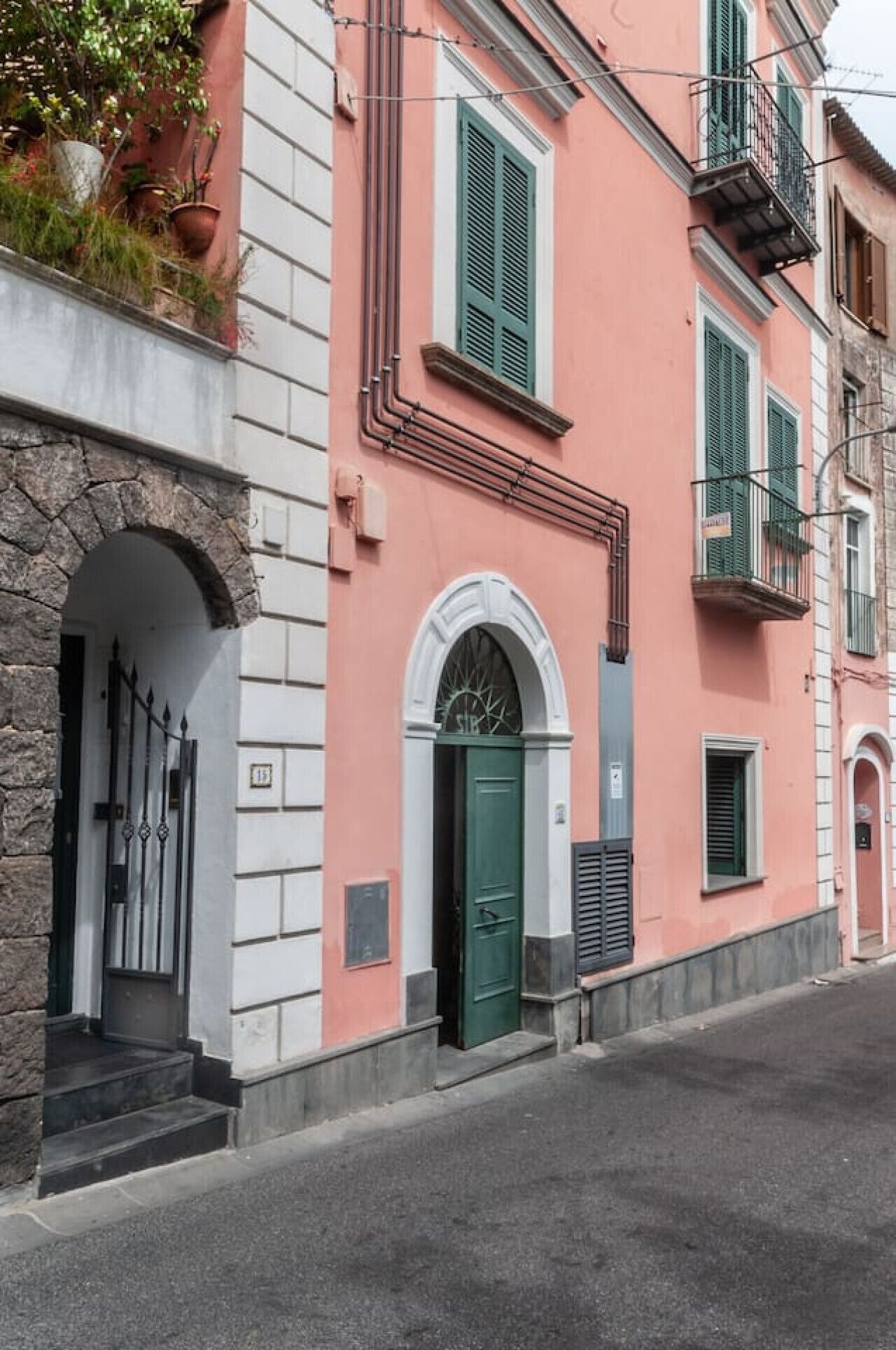 A pink building with a green door and shutters, stone archway, and a small balcony.