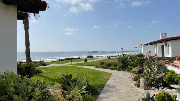 Un sendero que lleva a una playa con vista al océano y un muelle a lo lejos.