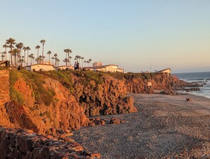 Zona costera con terreno rocoso, palmeras y edificios en un acantilado con vistas a la playa.