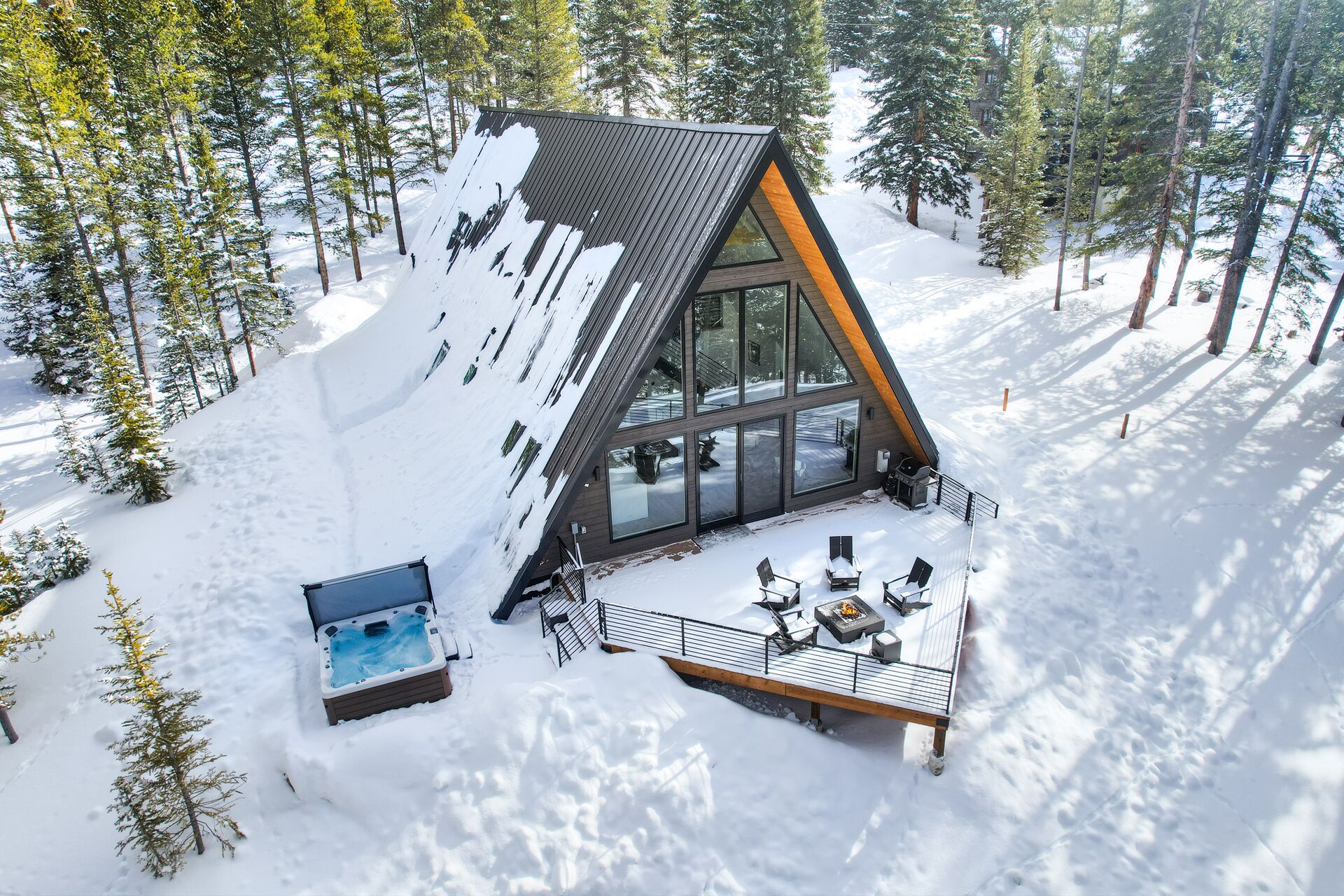 Una cabaña moderna con techo inclinado, ventanas amplias y una terraza con mobiliario exterior.