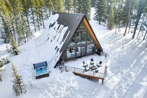 Una cabaña moderna con techo inclinado, ventanas amplias y una terraza con mobiliario exterior.