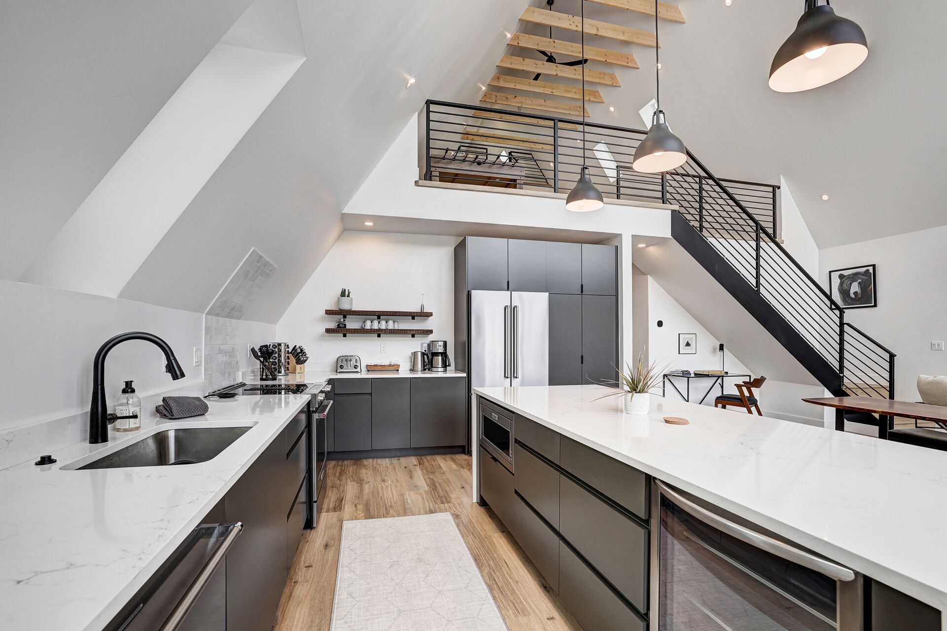 Une cuisine moderne dotée d’un îlot central, d’un coin repas avec une table et des chaises, et d’un escalier menant à un niveau supérieur.