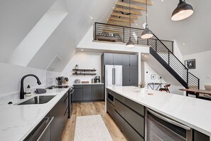 Una cocina moderna con una isla central, un área de comedor con mesa y sillas, y una escalera que conduce a un nivel superior.