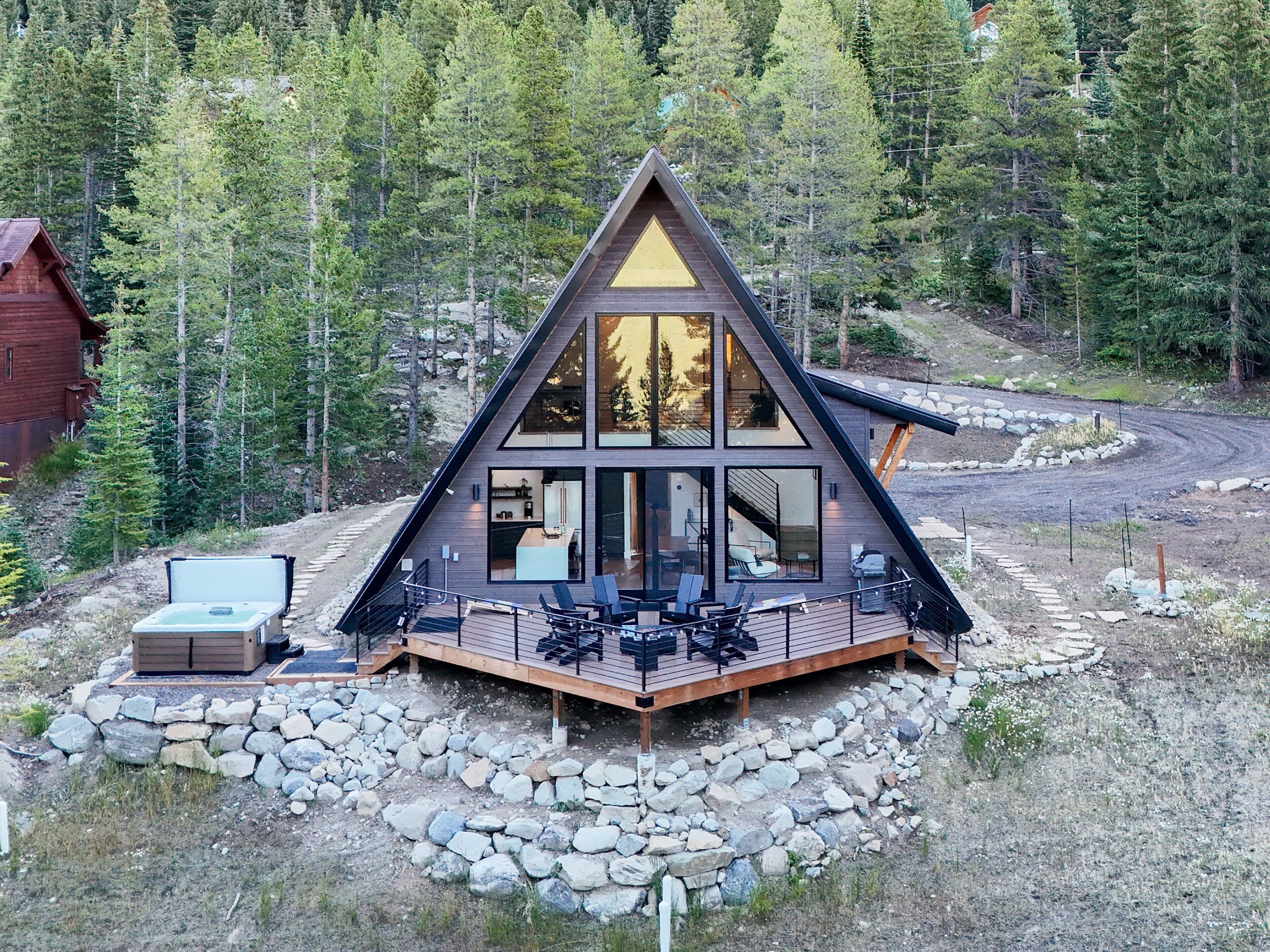 A modern cabin with a large deck, surrounded by a forest.