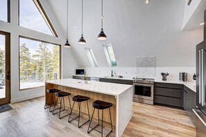 Una cocina moderna con una isla grande, taburetes de bar, horno empotrado y vistas a árboles.