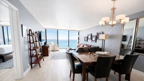 A modern hotel room with a dining area, a large window overlooking the sea, a chandelier, and a bed with a view. - Ocean View Luxury Condo (San Diego)