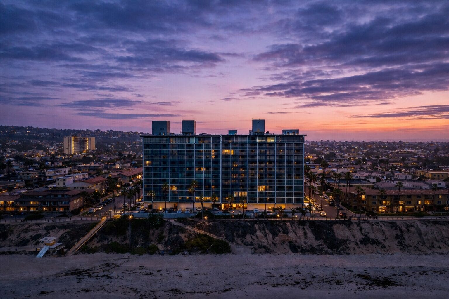 Un hôtel à plusieurs étages, doté d’une façade à motifs géométriques, situé près d’une plage au rivage rocheux.