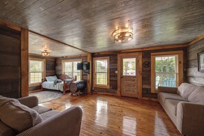 A rustic cabin interior with a wooden floor, a bed, a barrel, and a couch.