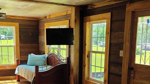 A spacious room with wooden floors, a bed, a television, and large windows.