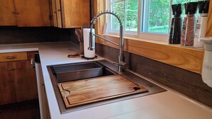 A kitchen with wooden cabinets, a stainless steel sink, and a window with a view of greenery.