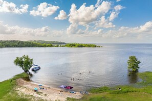 A lakeside view with boats, a sandy beach, and a forested island.