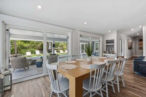 Uma ampla área de refeições com uma mesa grande e cadeiras, uma porta de vidro que dá para um pátio externo e um design de interiores moderno.