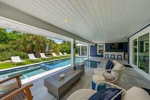 Uma área moderna de piscina ao ar livre com espreguiçadeiras, bar e um espaço de estar com almofadas.