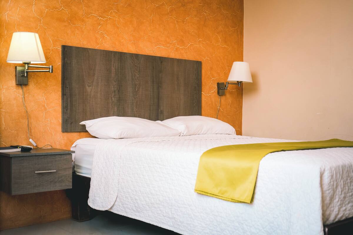 Habitació d'hotel amb un llit, una tauleta de nit i dues làmpades de paret.